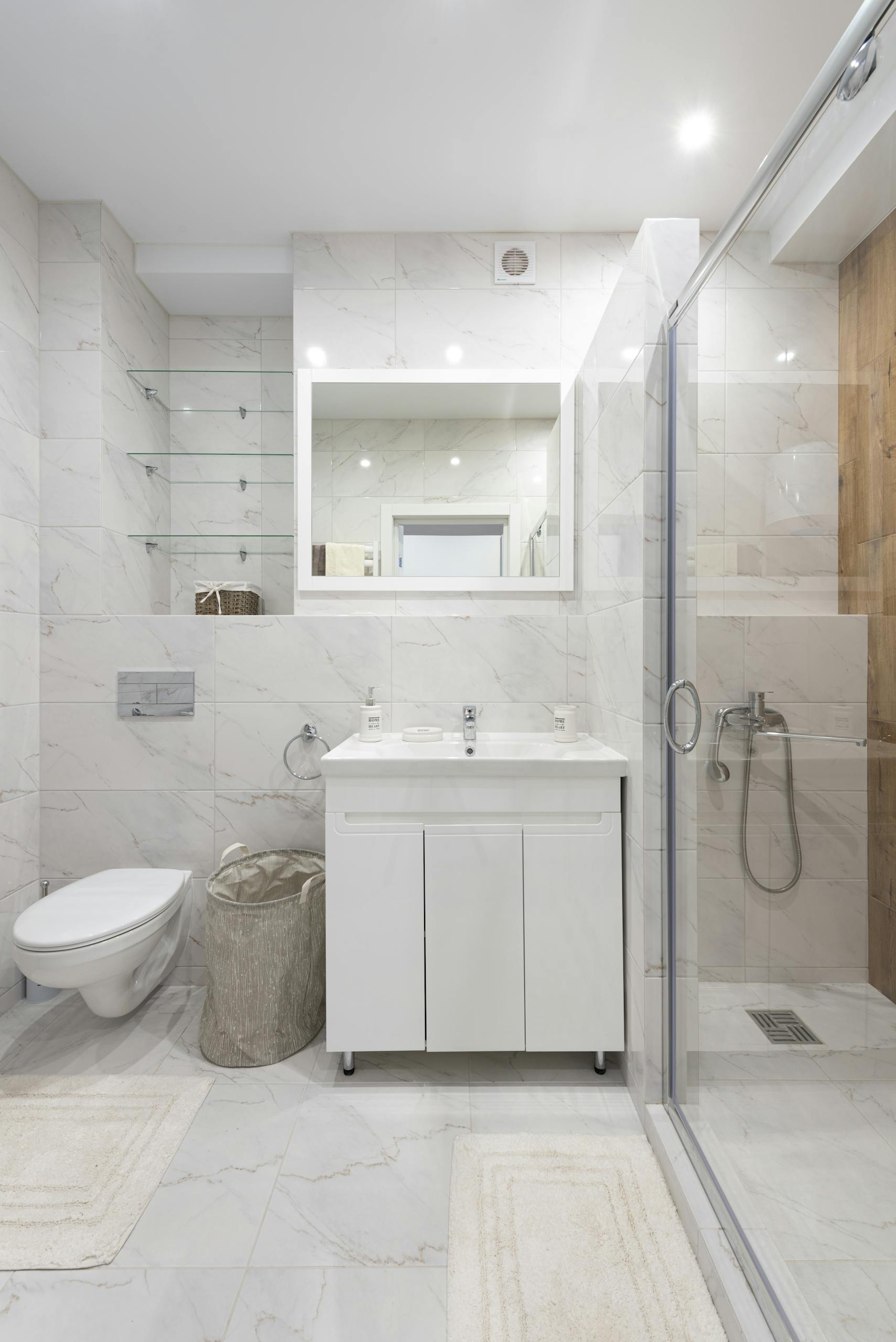 Contemporary bathroom with toilet bowl against cloth basket and washstand under mirror with shiny lights in house
